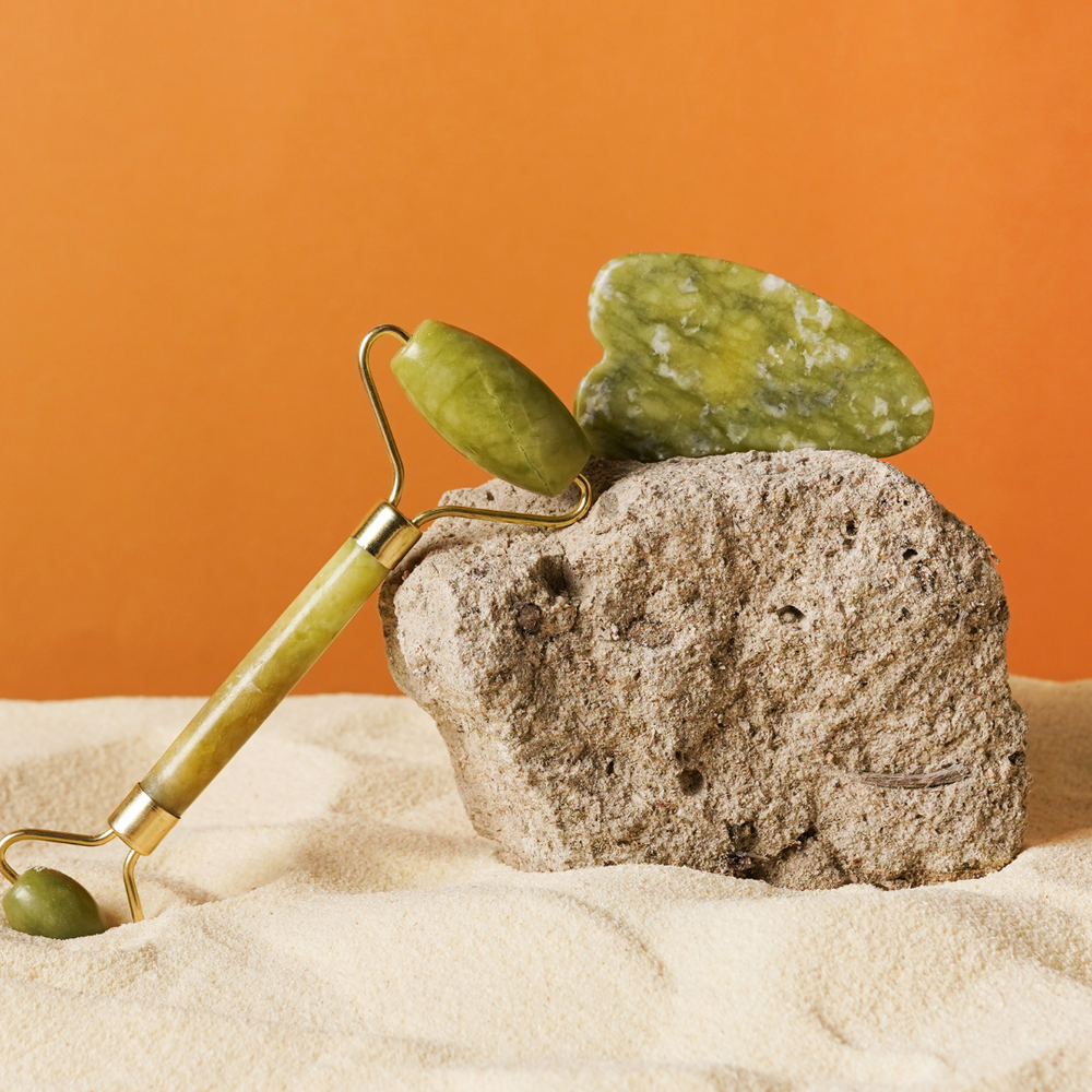 A Jade face roller and a Gua Sha stone lean against a stone