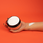 Hand holding jar of cream with swatch on arm.